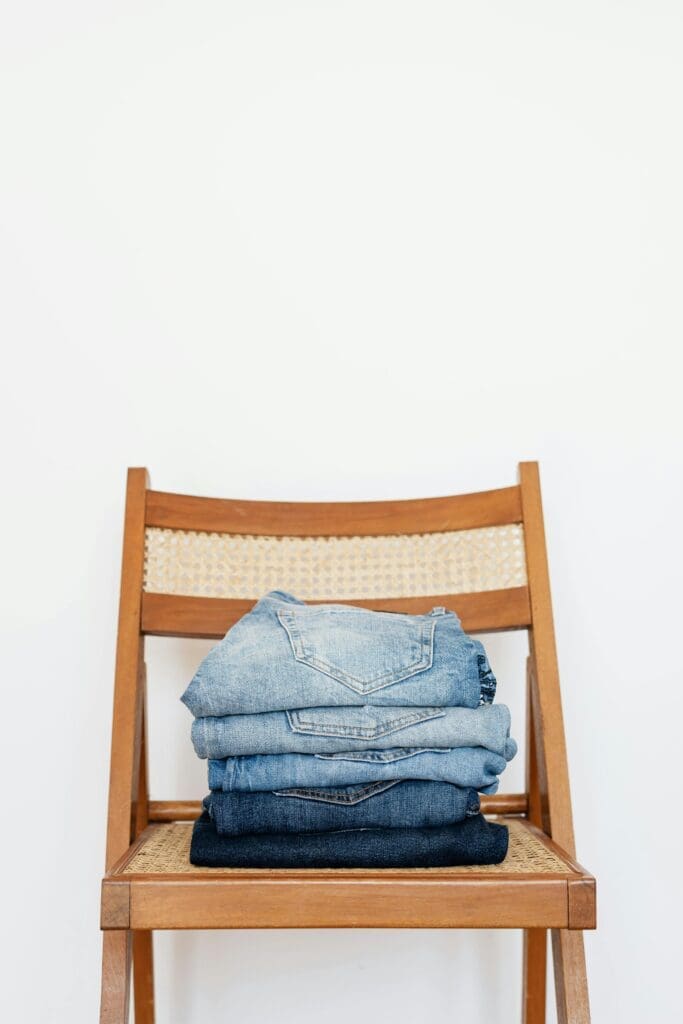 Denim neatly folding on Scandinavian minimalist chair with white backdrop.