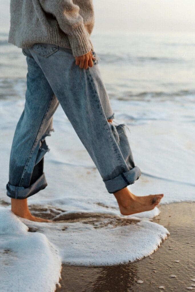 Woman walking barefoot on beach in loose denim waist down only.
