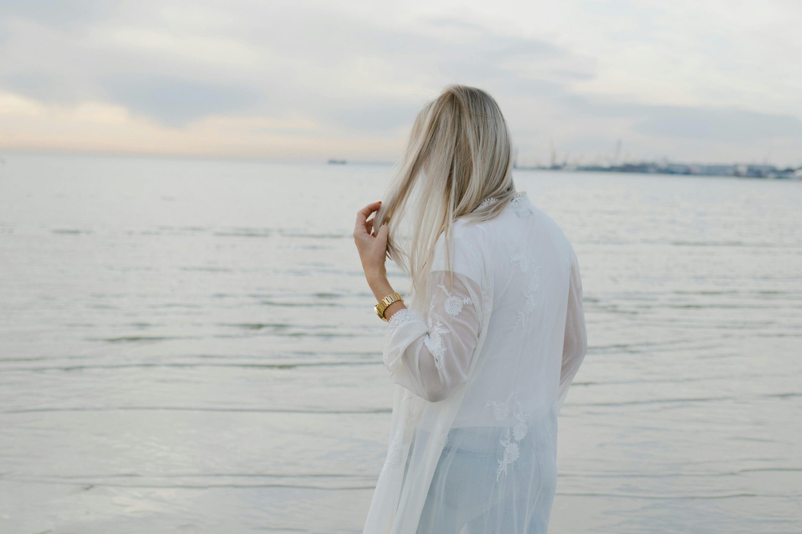 Blonde woman in white shirt standing by the ocean, minimal coastal scene. Coastal minimalist. Scandinavian Style.